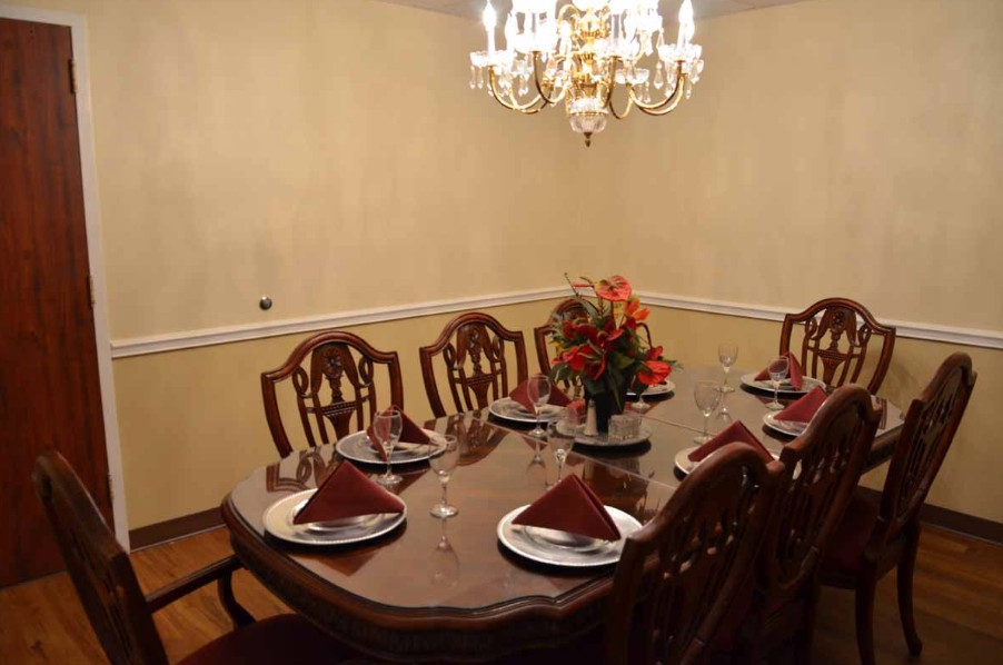 An elegantly set dining room table with a chandelier overhead and floral centerpiece.