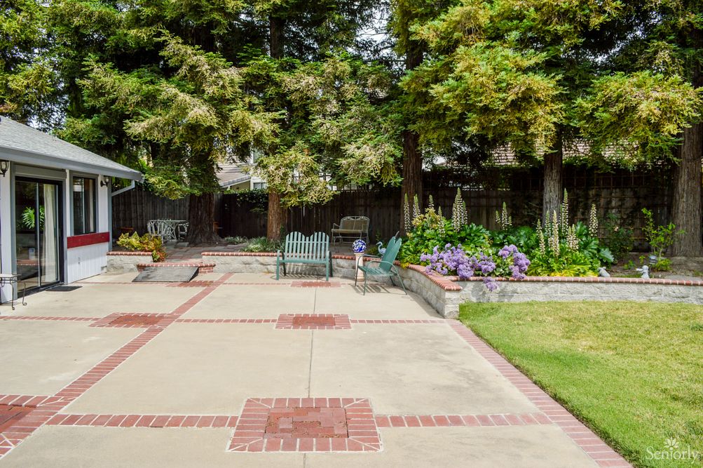 A spacious backyard patio area with outdoor seating, surrounded by trees and a flower garden.
