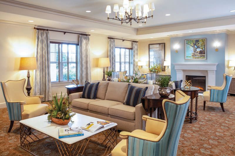 A well-decorated living room featuring a sofa, chairs, coffee table, and a fireplace under a chandelier.