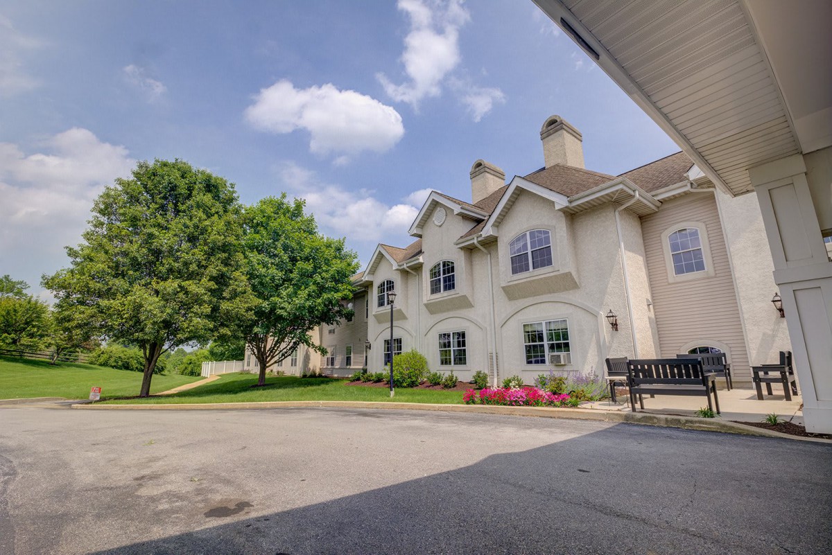 A residential building with well-maintained landscaping and a bench under a partly cloudy sky.