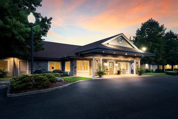 A well-lit building entrance at sunset with a neatly landscaped surrounding.