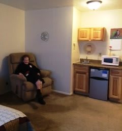 Woman sitting in a recliner in a small apartment with a kitchenette.
