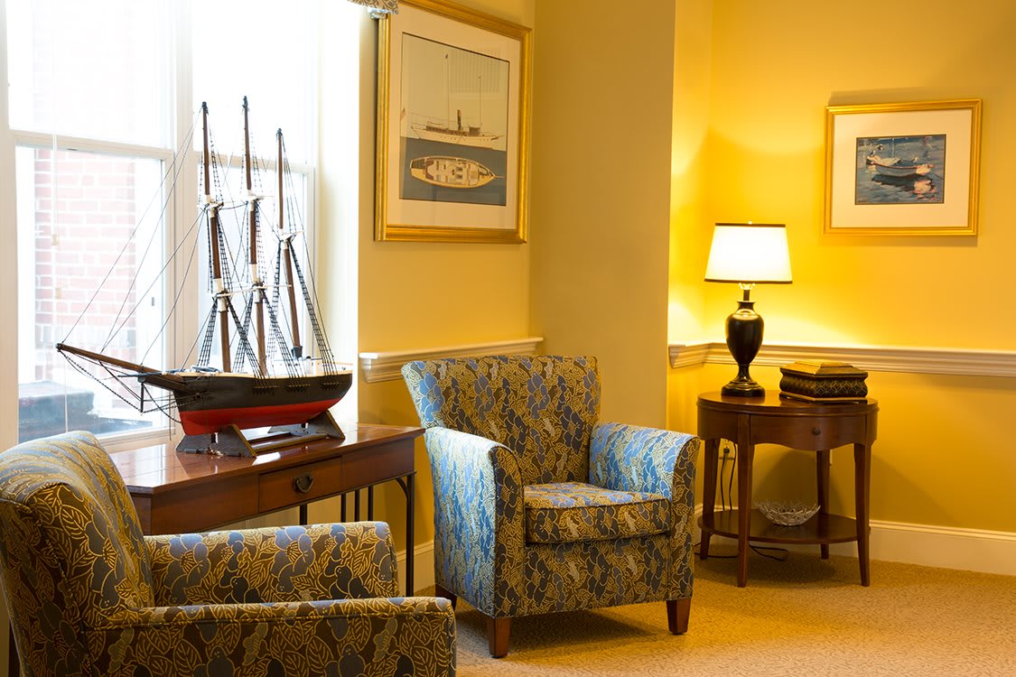 A cozy living room with armchairs, a lamp, and nautical-themed decor including a model ship and paintings.