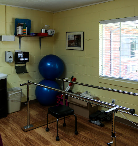 A well-equipped physical therapy room featuring parallel bars, a blue exercise ball, and ample natural light.