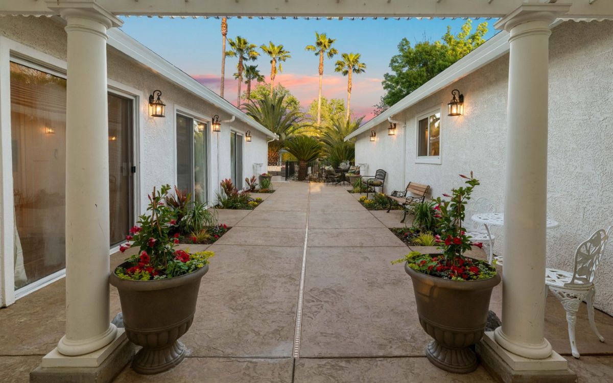 A serene courtyard with potted plants and palm trees visible against a sunset sky.