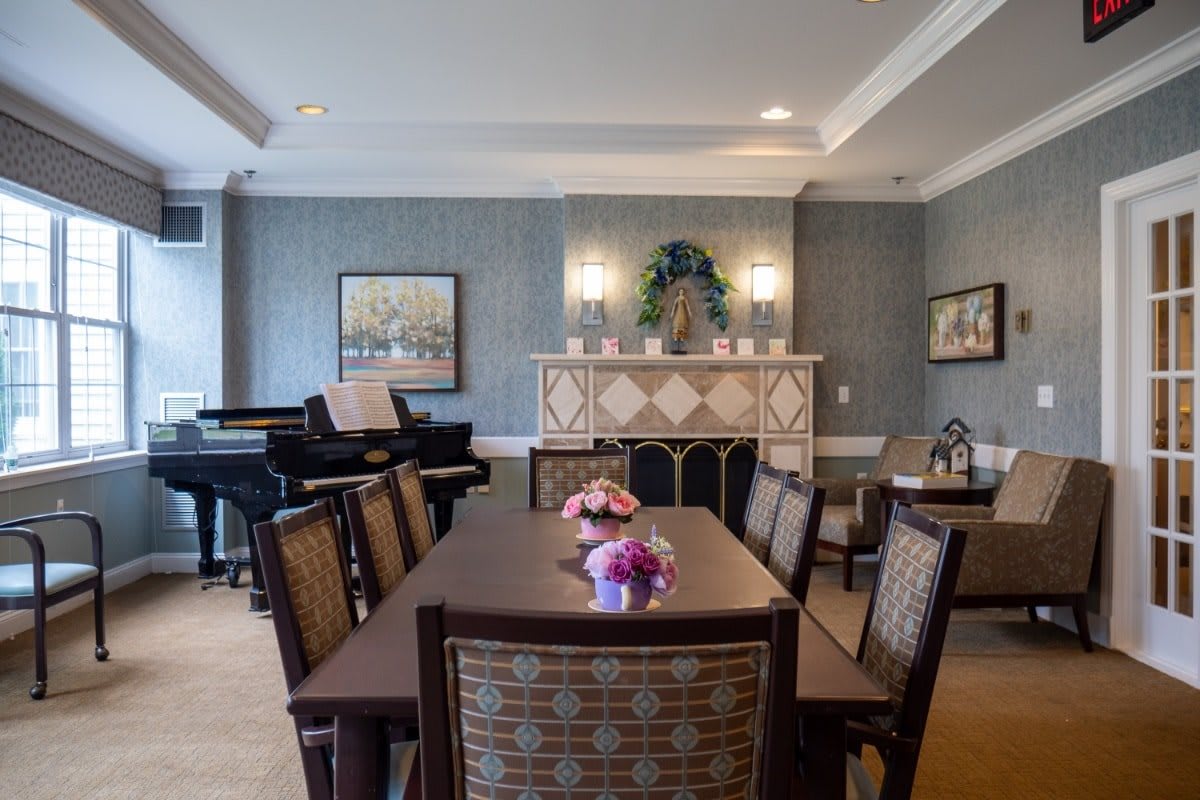 A well-decorated dining room with a wooden table and chairs, featuring a piano and elegant wall decor.