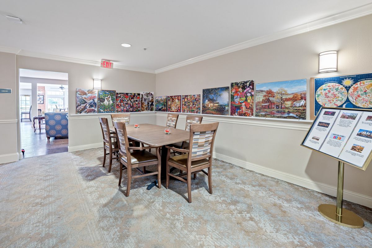A dining room featuring a large wooden table with six chairs, surrounded by colorful artwork on the walls.