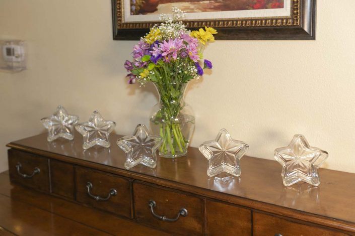 A bouquet of colorful flowers in a vase on a wooden dresser, surrounded by crystal star ornaments.