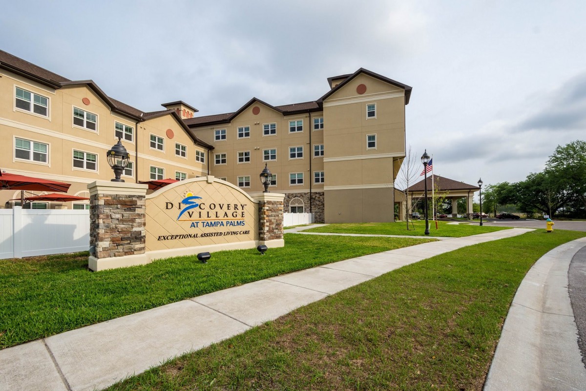 Exterior view of a multi-story residential building with a landscaped area and signage.