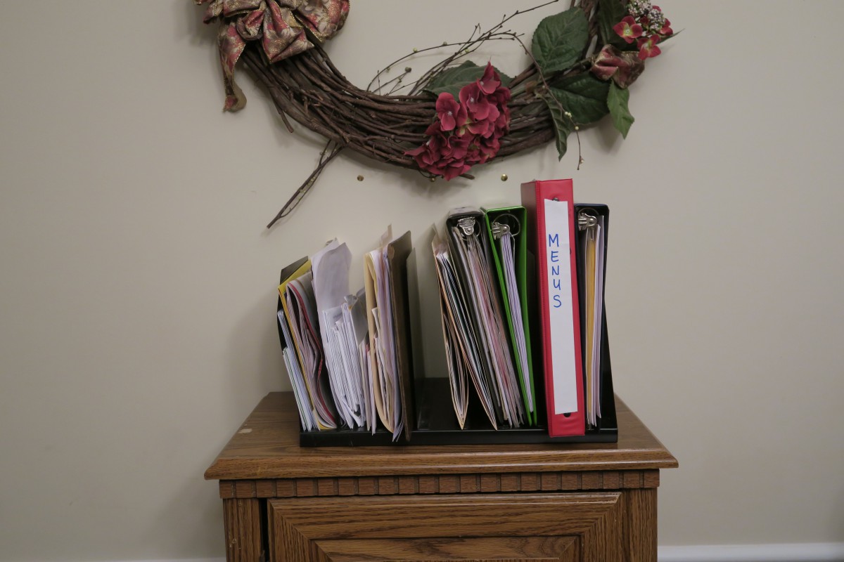Organized files and binders on a wooden table beneath a decorative wreath.