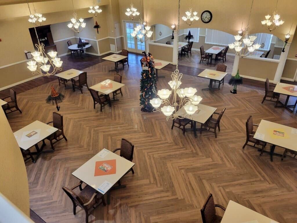 An overhead view of a spacious dining area with elegant chandeliers, neatly arranged tables and chairs on a wooden floor.