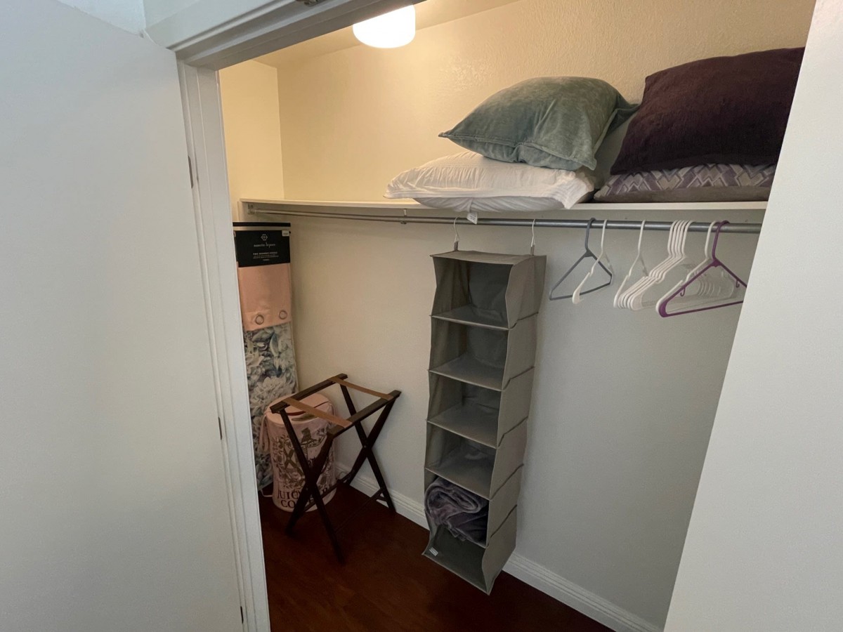 A small closet with shelves, hangers, and a luggage rack for organized storage.