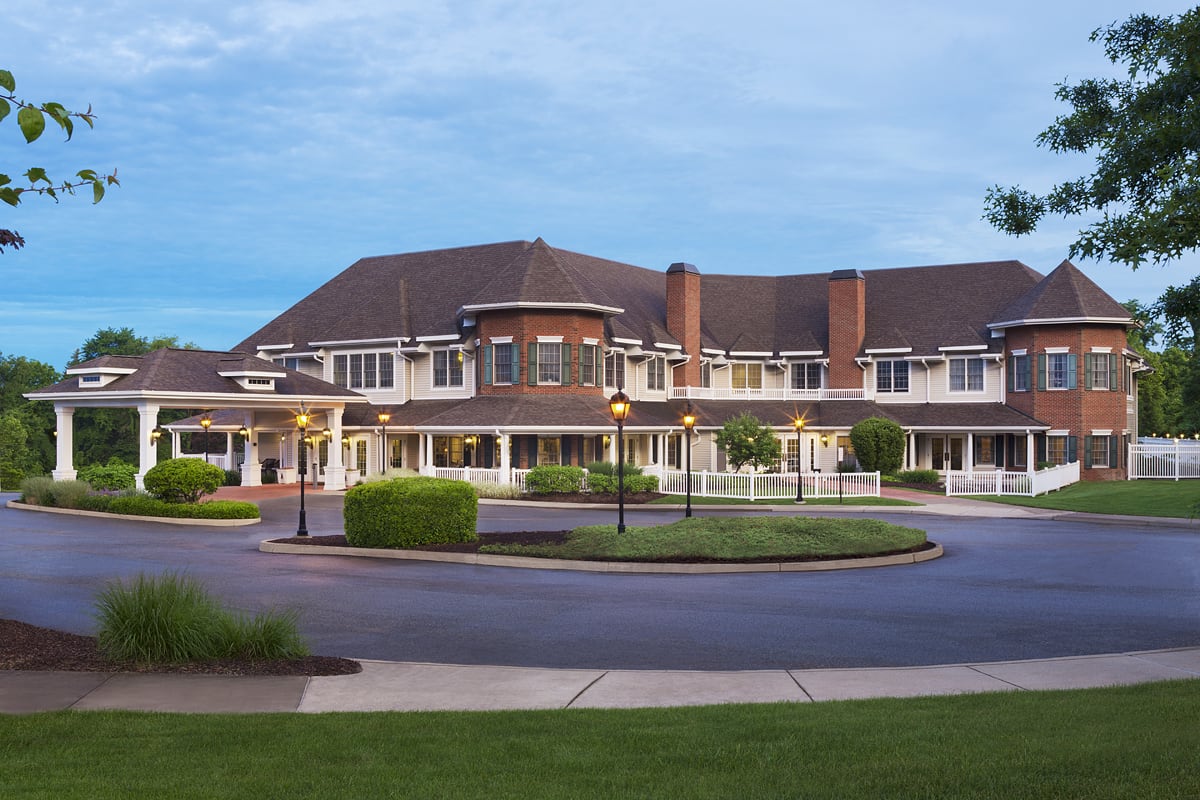 A large building with a circular driveway and illuminated lamps in the evening.