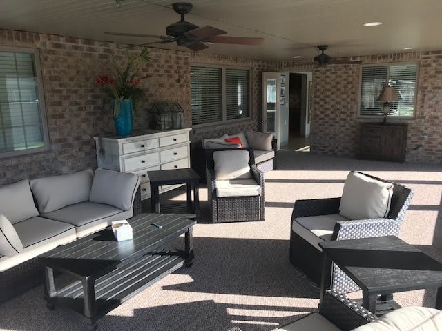 A comfortable outdoor patio with rattan furniture and ceiling fans, featuring a seating area against a brick wall.