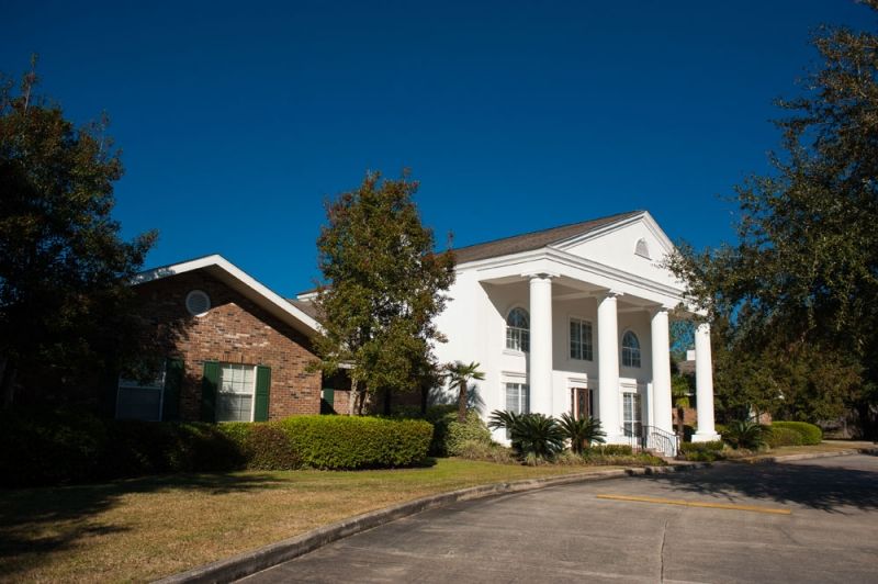 A suburban residential house with prominent white columns and a well-maintained lawn under a clear blue sky.
