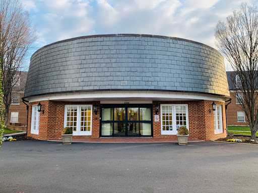 A modern circular building with large windows and a sleek roof, set against a cloudy sky.