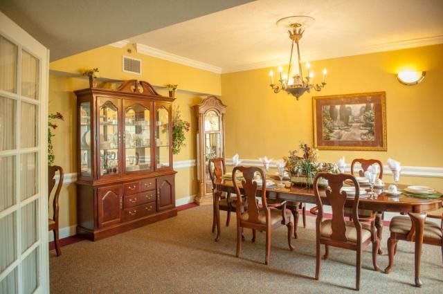 A classic dining room with a wooden table, matching chairs, and a chandelier, featuring yellow walls and a display cabinet.