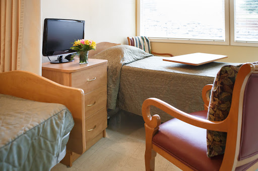 A cozy hospital room featuring two beds, a television, and a nice bouquet of flowers.