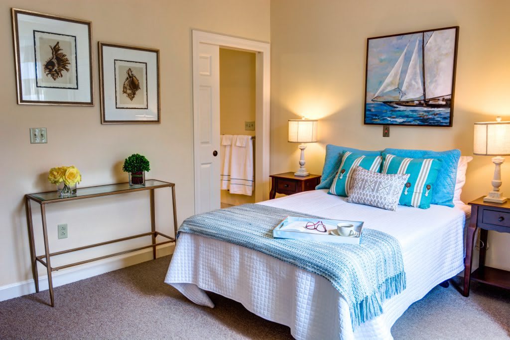 A cozy bedroom with nautical-themed decor, featuring a neatly made bed, artwork, and warm lighting.
