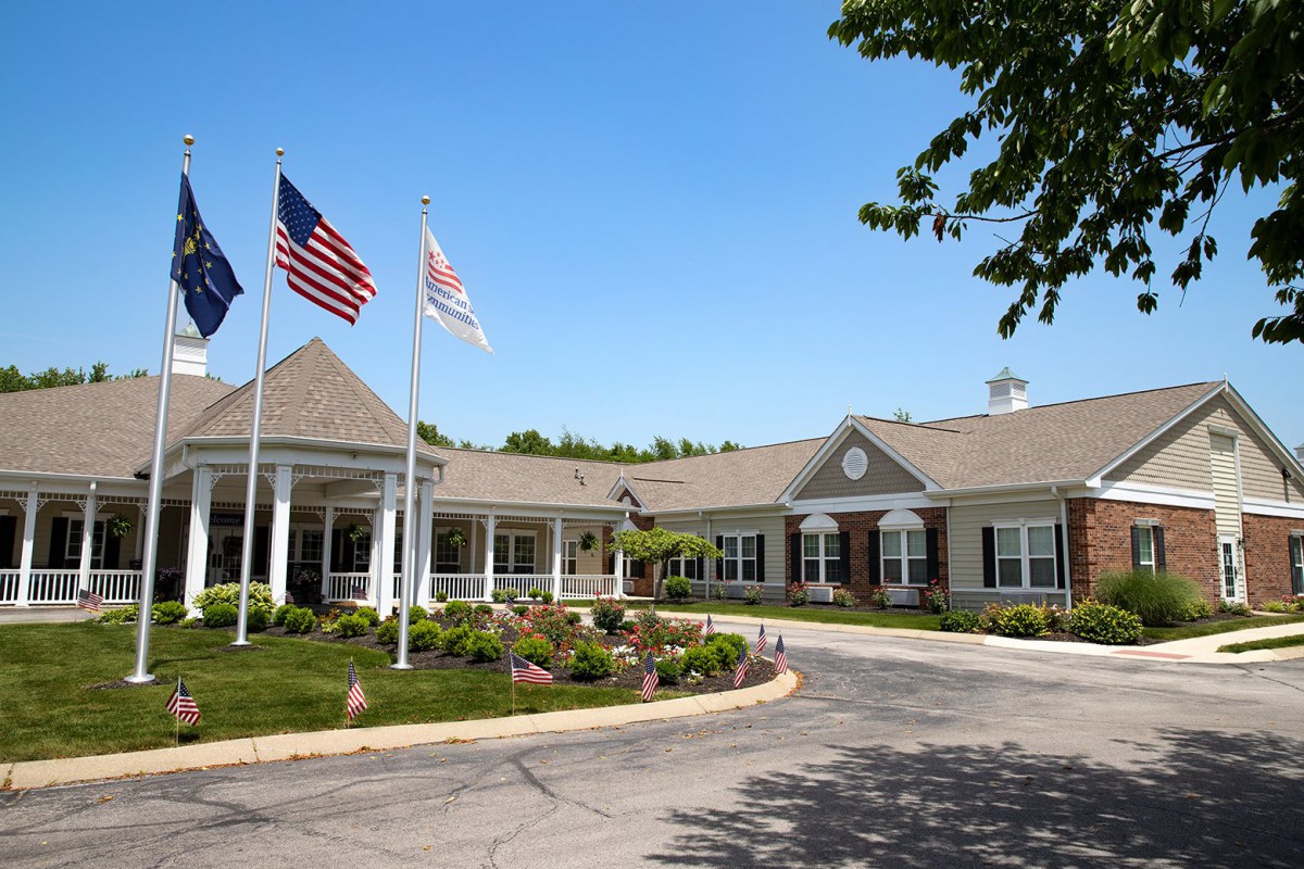 A single-story building with neatly maintained landscaping and multiple flags flying out front on a sunny day.