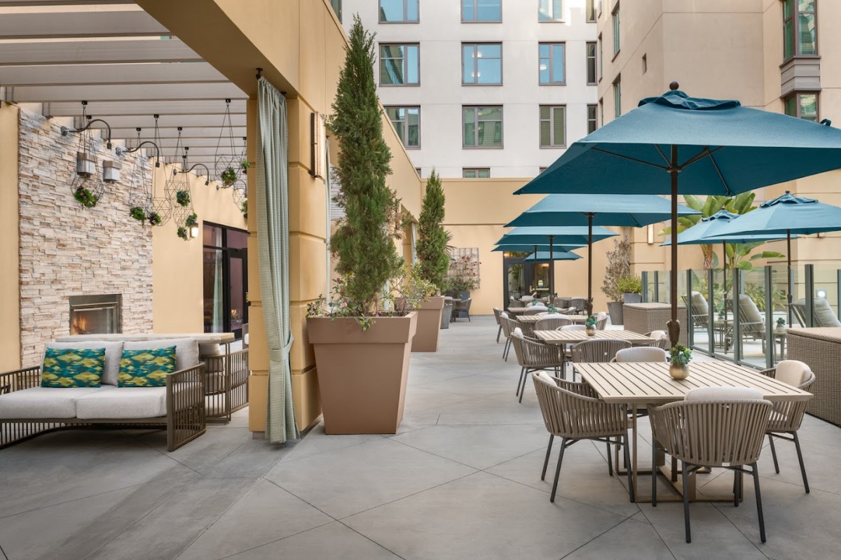 An inviting outdoor patio with tables and umbrellas, surrounded by plants in a courtyard setting.