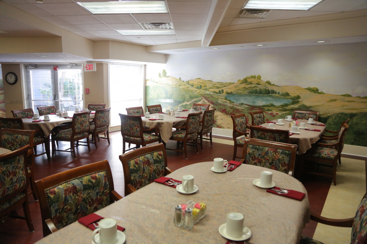 A restaurant dining area with tables set for service and a scenic mural on the wall.