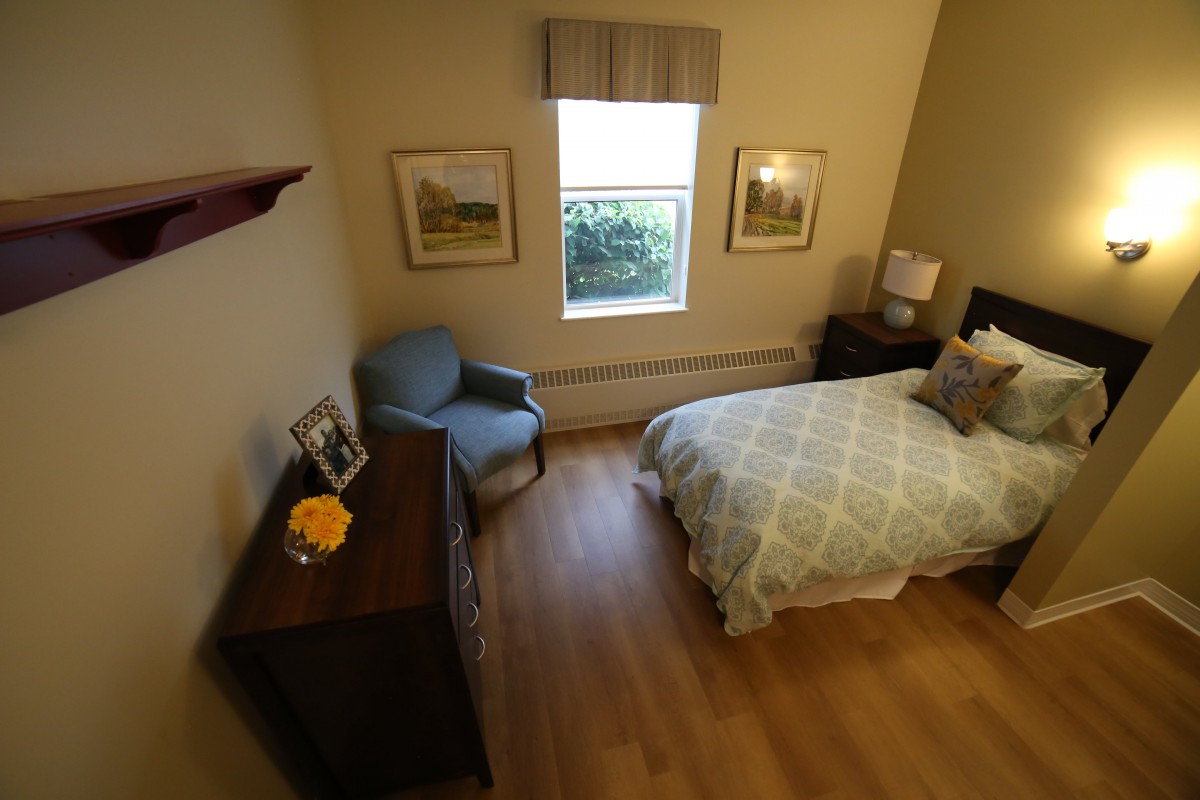 A cozy bedroom featuring a bed, chair, dresser, and window with wall decorations.