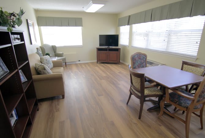 A bright living room with wooden flooring, furnished with chairs, a table, and a television.