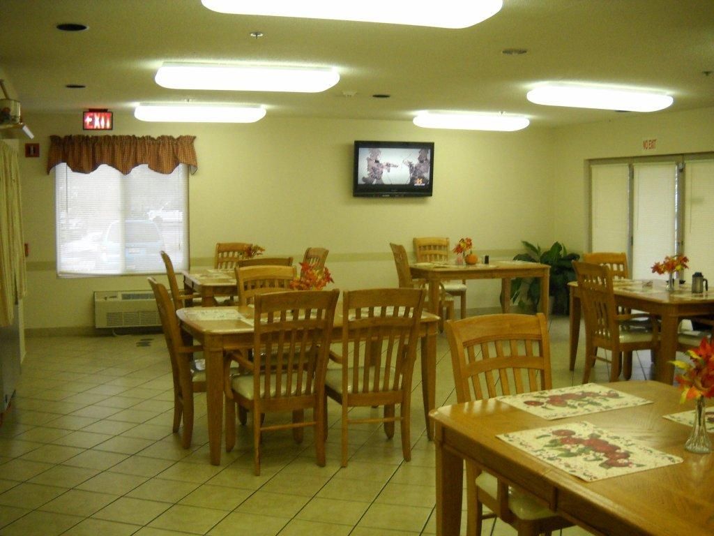 An empty dining area with wooden tables and chairs, featuring a television on the wall.