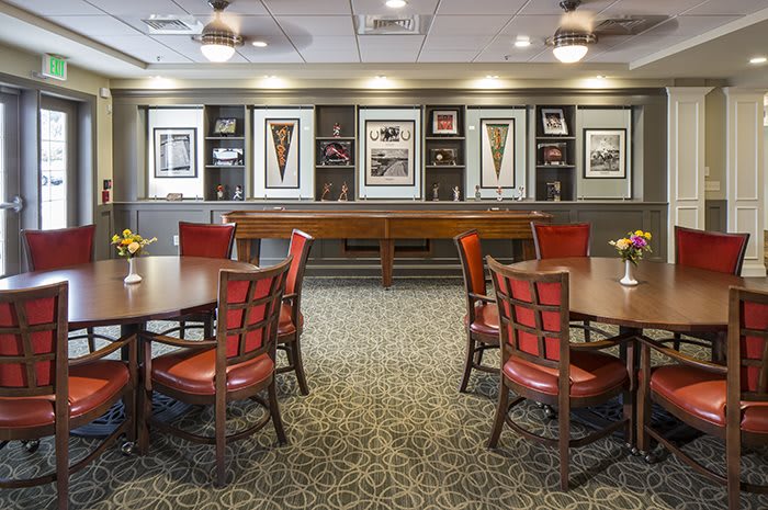 A cozy interior with red chairs and round tables, decorated with framed art on the walls.