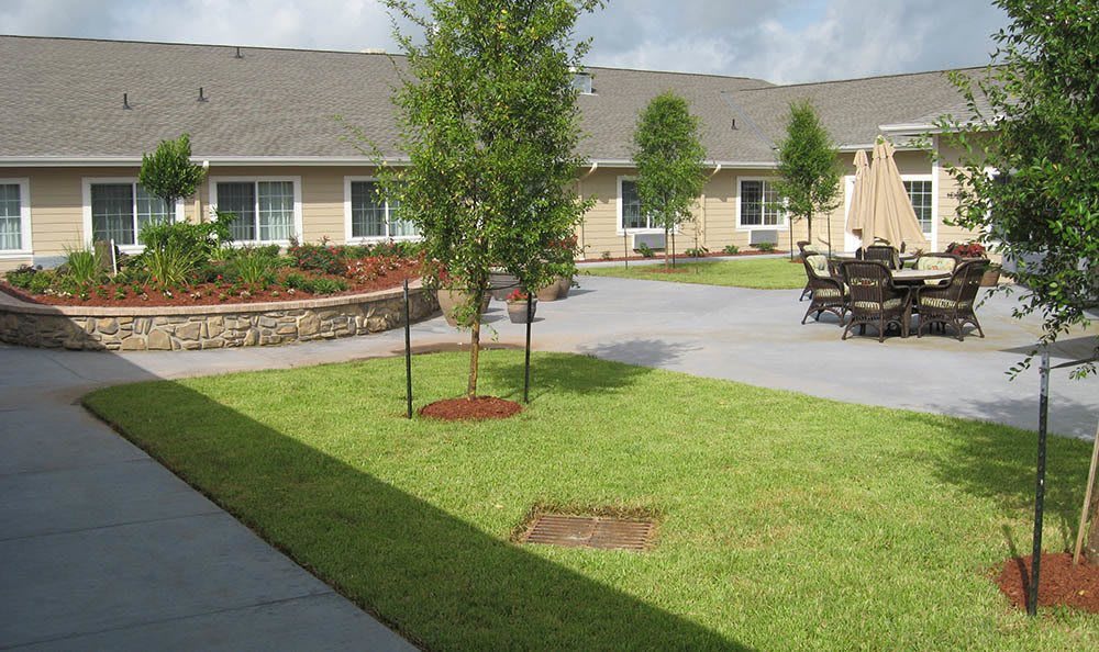 A well-maintained courtyard with a grassy lawn, young trees, and outdoor seating surrounded by a building.