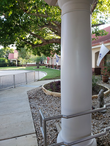A view of a pathway leading to a building, framed by a column and surrounded by greenery.