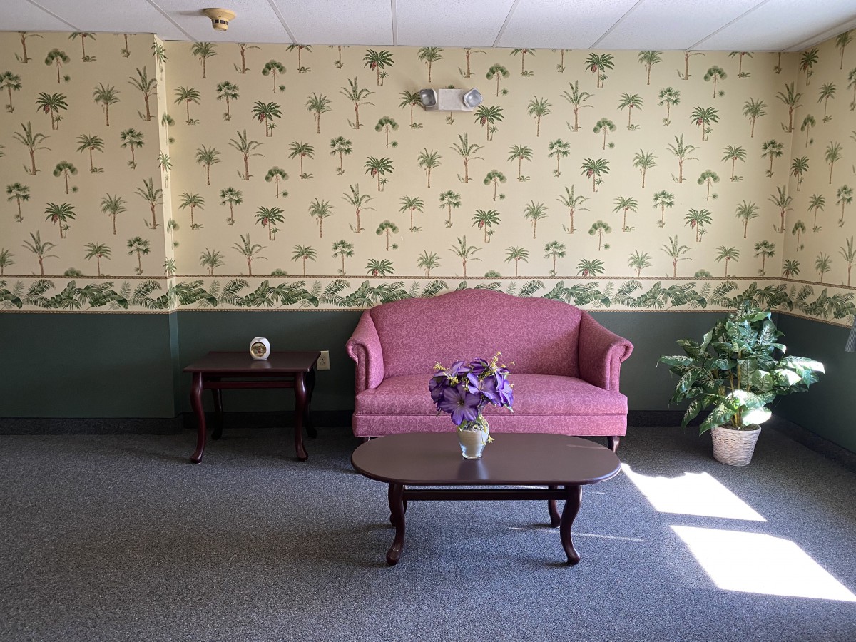 A cozy living room with a pink sofa, a wooden coffee table holding a vase of flowers, and decorative wallpaper.