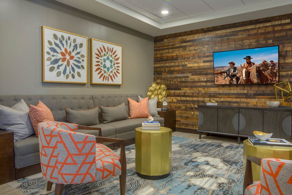 A modern living room with stylish furniture and decor, featuring a wooden accent wall and colorful artwork.