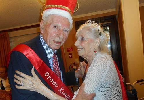 An elderly couple joyfully dancing, adorned with prom king and queen attire.