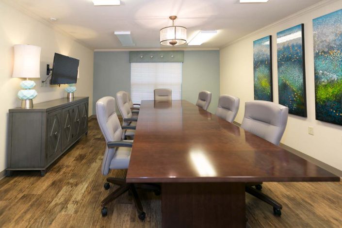 A modern conference room with a long wooden table and upholstered chairs.