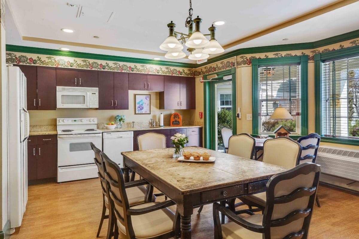 A cozy kitchen and dining area with a wooden table, chairs, and classic appliances, accented by decorative molding and green trim.