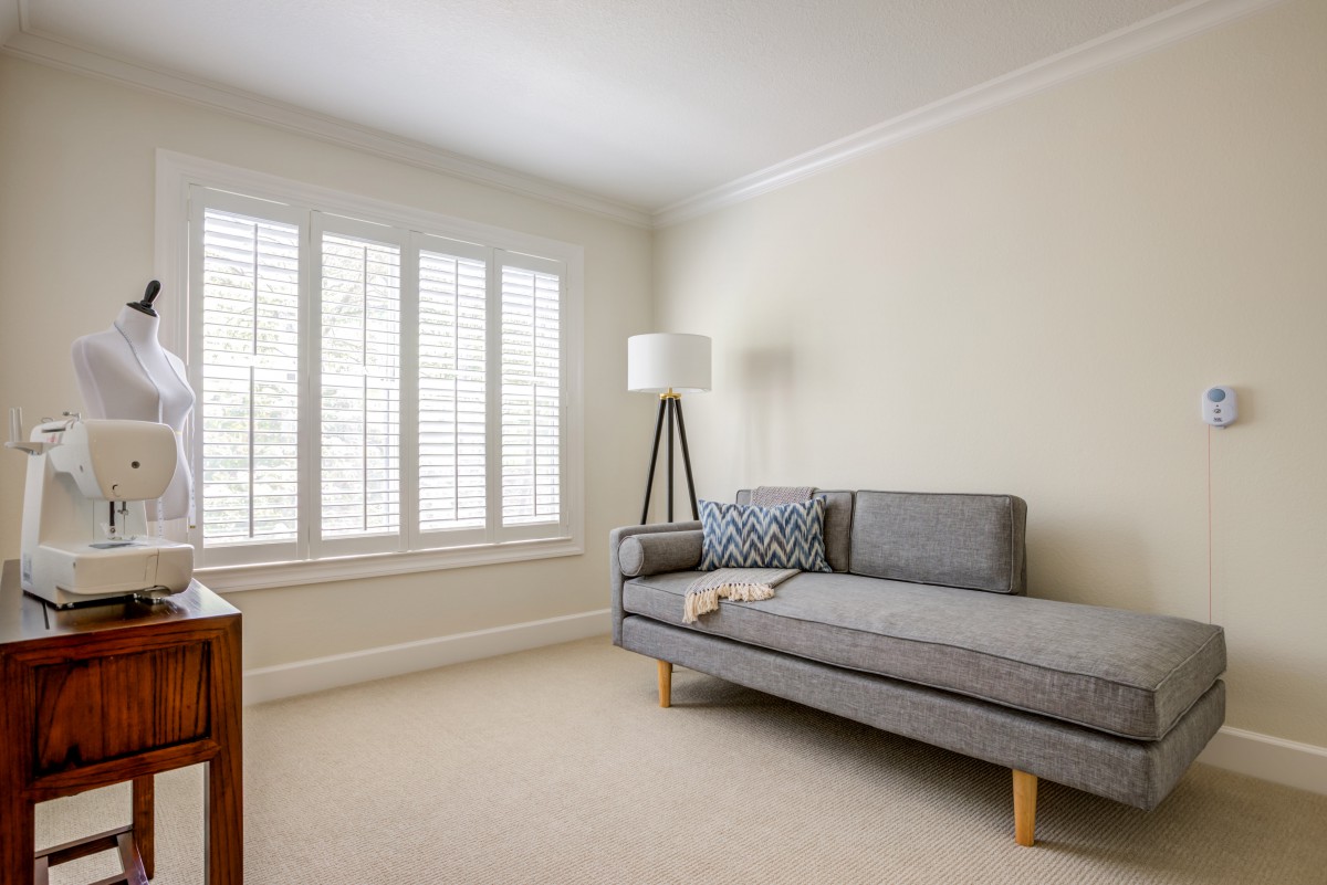 A minimalist living room with a gray sofa, floor lamp, and window shutters.