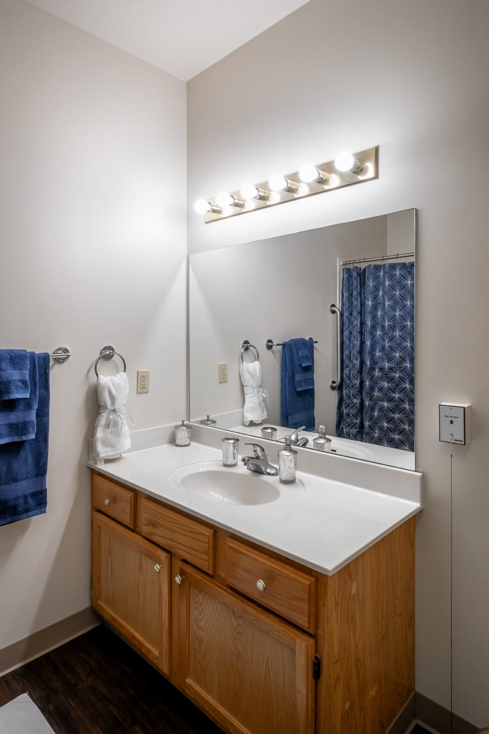 A well-lit bathroom with a wooden vanity, large mirror, and blue towels.
