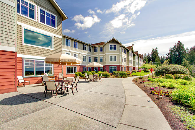 An exterior view of a large residential building with a landscaped garden and outdoor seating area.