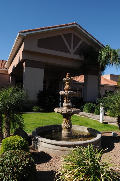 A picturesque fountain in front of a building surrounded by lush greenery and palm trees.