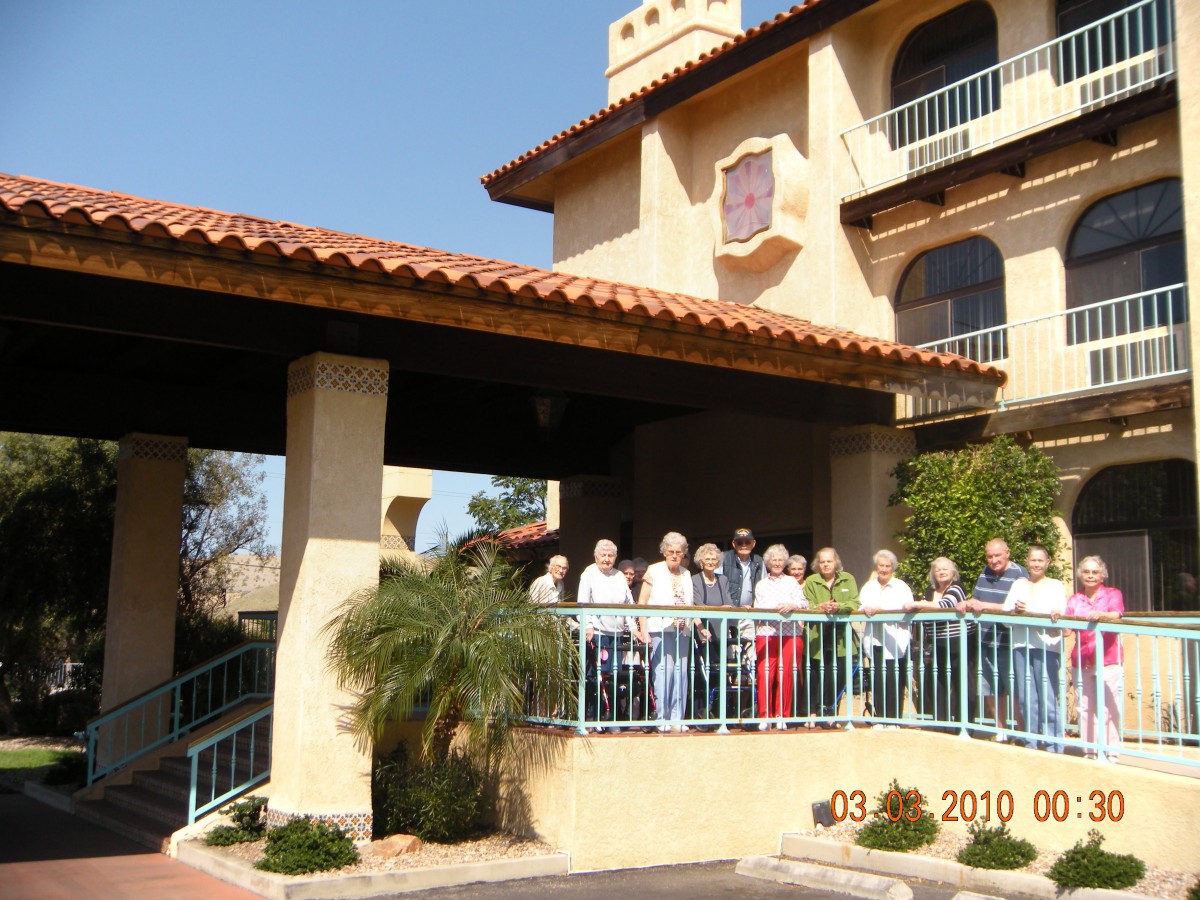 A group of people standing on a balcony in front of a Mediterranean-style building.