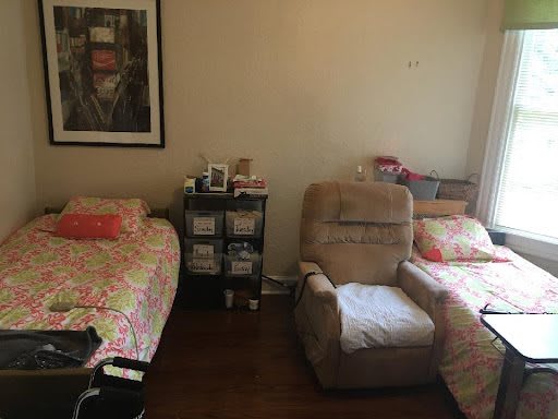 A cozy bedroom with twin beds, an armchair, and a framed picture on the wall.