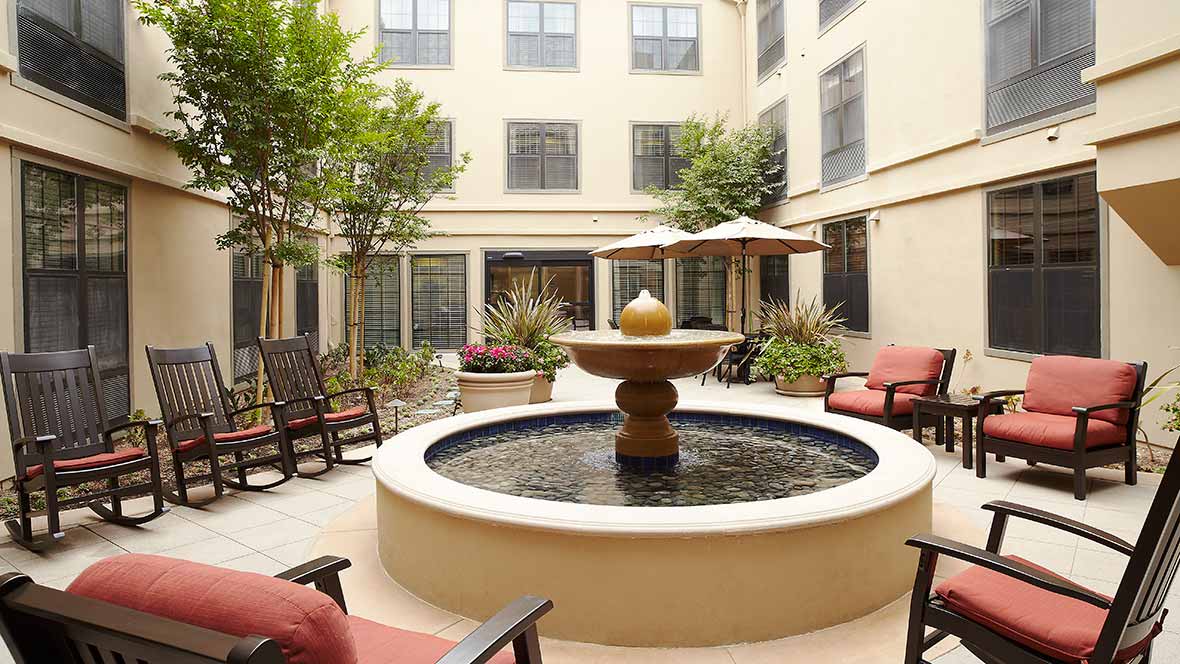 A serene courtyard featuring a central fountain surrounded by comfortable seating and lush greenery.