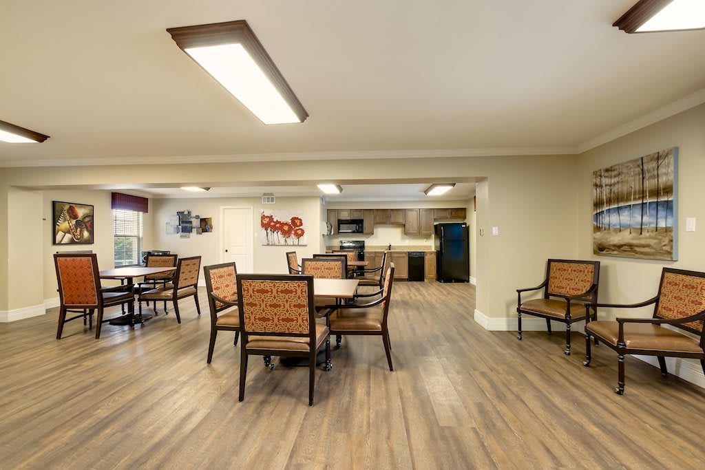 A spacious dining room with wooden tables and chairs, adjacent to a kitchen area.