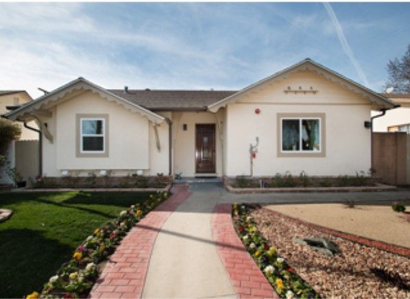 A charming single-story house with a brick pathway leading through a landscaped garden.