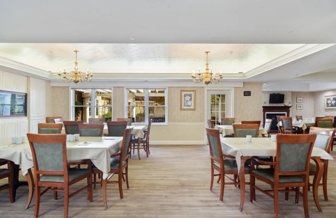 A well-lit dining room with neatly arranged tables and chairs, featuring elegant chandeliers.