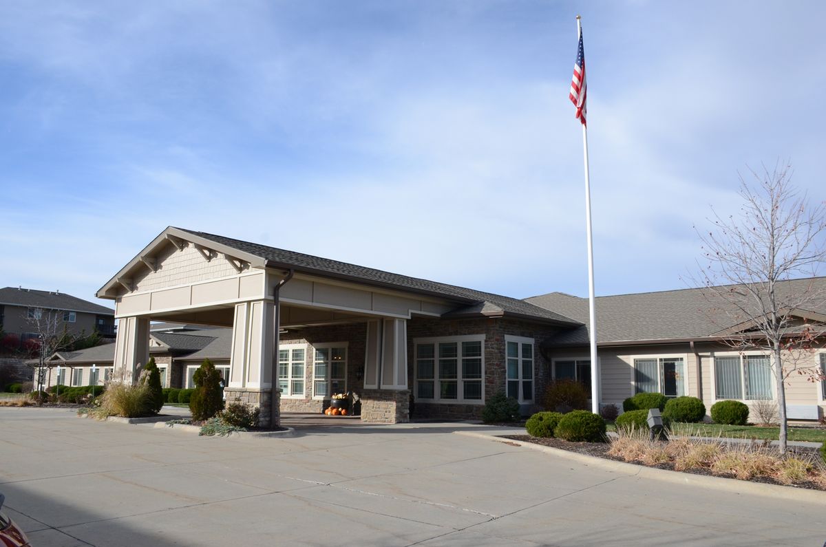 An exterior view of a building with an American flag raised on a flagpole, featuring a landscaped entrance under a clear sky.