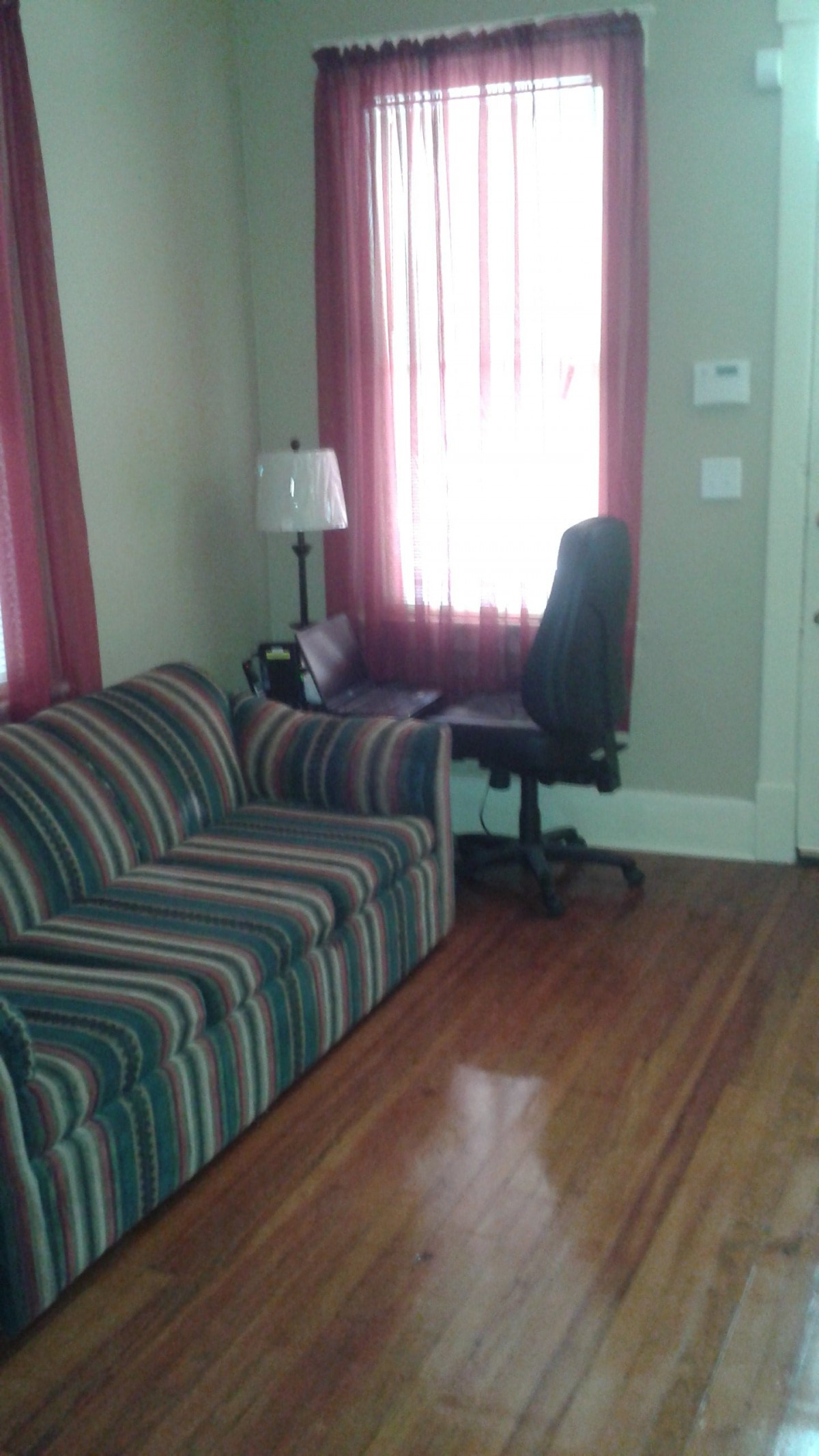 A cozy living room with a striped couch, a desk chair by the window, and wooden floors.