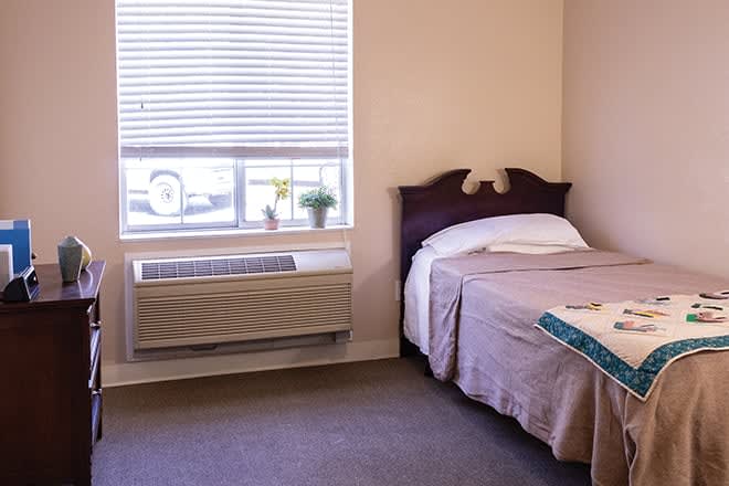 A cozy hotel room with a single bed next to a window and air conditioning unit.